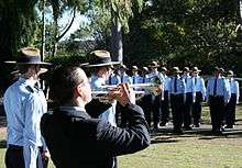 Photograph of a trumpeter in the foreground, with uniformed Air Force Cadets in the background, on the St John's site