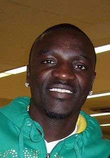 A black man, wearing a green hooded top and white shirt, smiles into a camera.