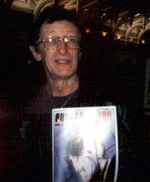 A photograph portrait of a man holding a comic book.