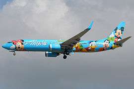 Left side view of a light blue aircraft adorned with Mickey Mouse and other Disney characters, with dark clouds in the background.