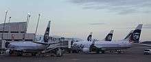 Early morning photo showing Alaska Airlines aircraft parked at an airport terminal, with jetways connected to the planes. Five aircraft can be seen in the photo.