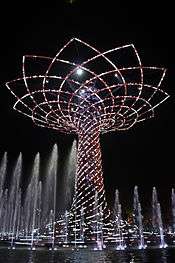 Large tree made of lights at night, surrounded by fountains