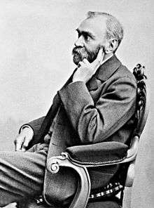 A black and white photo of a bearded man in his fifties sitting in a chair.