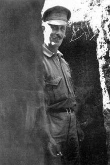 Informal photograph of a man in military uniform leaning against the wall of a trench.