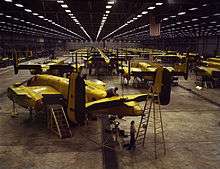 Interior of huge aircraft factory where rows of bombers are being assembled.