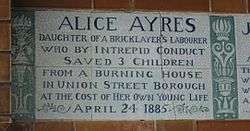 A tablet formed of six standard sized tiles, bordered by green flowers in the style of the Arts and Crafts movement. The tablet reads "Alice Ayres, daughter of a bricklayer's labourer who by intrepid conduct saved 3 children from a burning house in Union Street, Borough, at the cost of her own young life April 24, 1885".