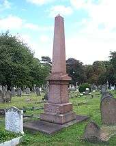 A tall red four-sided obelisk, surrounded by much shorter gravestones
