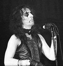 Black-and-white photo of a long-haired man in black makeup with a microphone