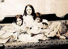 A black-and-white picture of three Victorian children sitting on a couch.