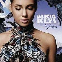 A young woman with her eyes closed, wearing a feathered dress that covers her chest, bares her shoulders and goes around her neck. Laid against a blue background, a white dove is seen flying behind her to the left. The name "Alicia Keys" is written to the right in white font and "The Element of Freedom" is written below that in dark blue font.