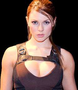 A close-up picture of a brunette woman dressed in a brown and black, sleeveless sports shirt.