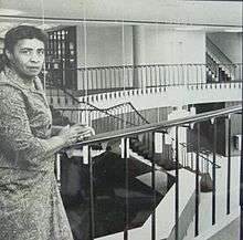 Black woman with short hair standing at a rail in a library second floor