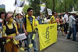 Gay-pride marchers on a street, with yellow banner and clothing