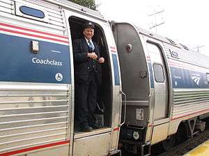 An Amtrak conductor standing in the doorway of an Amfleet cars with its trapdoor in the closed position