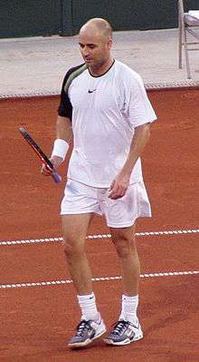 A man wearing white clothing looking at a tennis racket