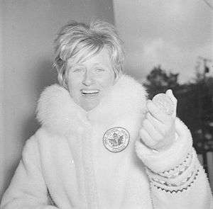 Anne Heggtveit wearing a plush coat, holds up a round medal.