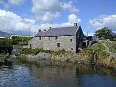Old, slate-roofed, grey stone mill building, situated beside a small river.