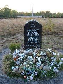 A Memorial for Margot and Anne Frank shows a Star of David and the full names and birthdates and year of death of each of the sisters, in white lettering on a large black stone. The stone sits alone in a grassy field, and the ground beneath the stone is covered with floral tributes and photographs of Anne Frank