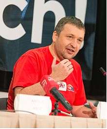 Middle-aged man in Red t-shirt talking in front of a microphone