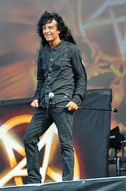 Smiling, casually-dressed singer with long, black hair onstage