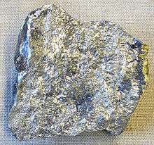 An irregular piece of silvery stone with spots of variation in lustre and shade.
