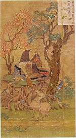 A priest seated under a tree feeding a four-legged animal in the shape of a small horse.