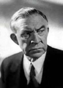 Black and white portrait photo of a white man wearing a suit and tie.