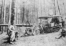 A field gun and crew, with Holt tractor, resting in a forest of very tall trees.