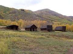 Four small old wooden houses seen at some distance with high hills in the background.