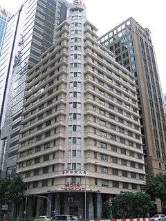  Beige rectangular building, 20 storeys and at 87 metres tall, with newer taller skyscrapers seen in the background.