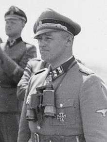 Black-and-white portrait of a man wearing a peaked cap, military uniform with an Iron Cross displayed at his neck.