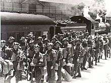 Soldiers in service dress uniform stand near a train