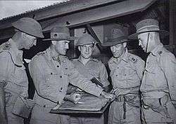 A group of military officers discuss plans around a map