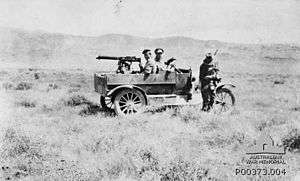 A Light Car Patrol in a landscape; driver standing beside front of car, passenger sitting in seat and machine gunner sitting in rear with gun