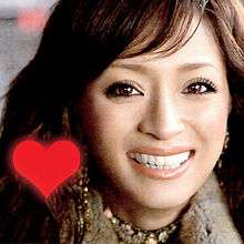 An up-close shot of Ayumi Hamasaki smiling and looking into the camera. On the lower left is a red heart.