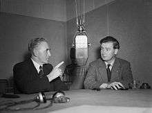 Iorwerth Thomas and Gwynfor Evans sitting at a table in front of a BBC microphone, debating.