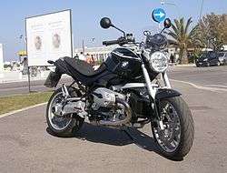Front three-quarter view of a black R1200R parked on a street with palm trees in the background