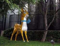 Statue with a stylistic representation of a deer in yellow and white with a blue ribbon around its neck.