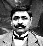 Black and white portrait photograph of a moustachioed man dressed in a dinner jacket and bow tie