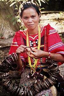 Native woman in a red decorated tribal blouse making tribal bracelets