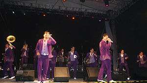 Two men with in purple jackets singing into a microphone