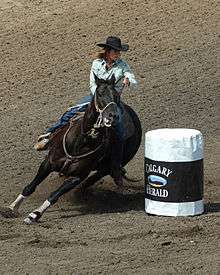 A woman on horseback makes a sharp turn around a white barrel.