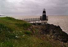 Metal lighthouse reached by walkway from land.