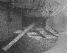 Underwater photograph of a gun protruding from an opening in the side of a sunken ship.