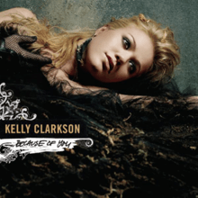 An image of a blonde Clarkson wearing black voluminous dress lying down with her head resting on her left hand, looking aside. At her right, the words "Kelly Clarkson" and "Because of You" are written in yellow and black capital letters respectively.