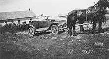Two people in an automobile hitched to two horses
