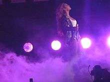 Beyoncé performing on stage, surrounded by stage smoke while purple stage lighting shines upon her.