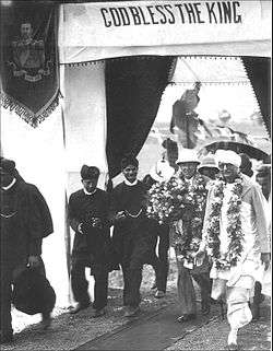A group of Western-clad Indians in turbans escort a Western dignitary holding a flower bouquet in hand