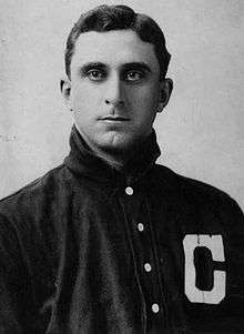 A close-up of a man wearing a dark baseball jersey with a white "C" on the left chest looking into the camera.