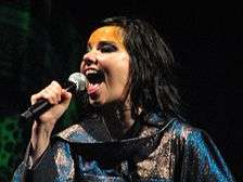 A woman wearing gold facepaint, singing into a microphone